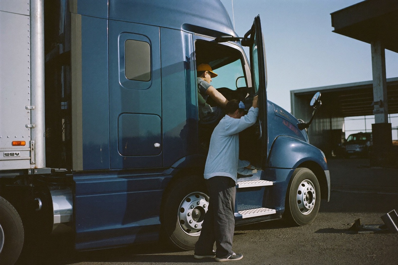 Drivers checking the cab of a semi truck at a freight depot at sunrise